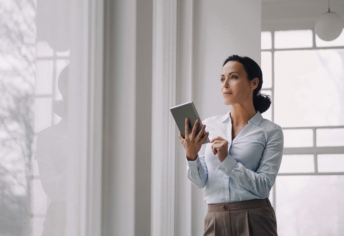 Woman holding a tablet, looking out a window