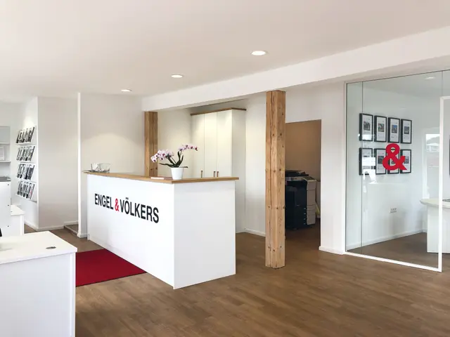 Engel & Völkers office interior with a white reception desk, wood floors, and a glass-walled office.