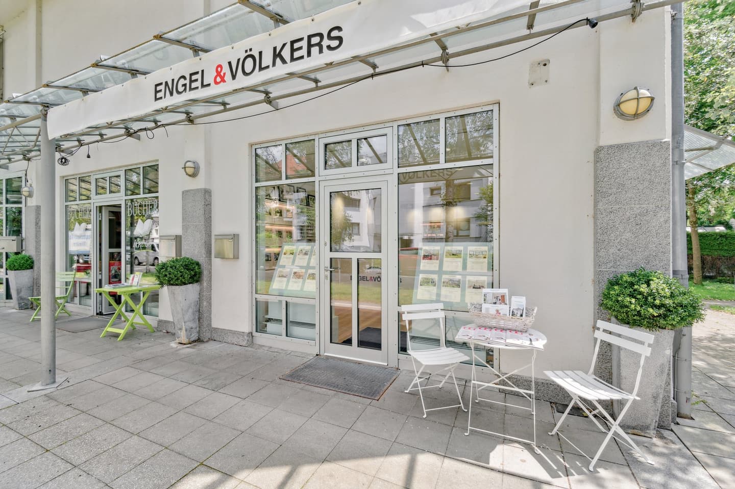Engel & Völkers real estate office exterior. White building with glass windows, tables, and chairs outside.