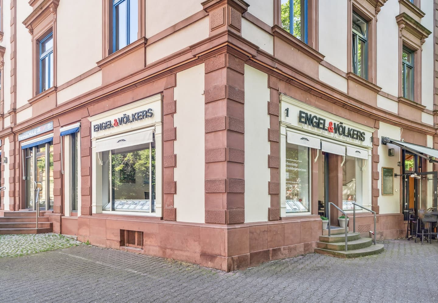 Engel & Völkers real estate office exterior. Glass windows display property listings. Steps lead to the entrance.