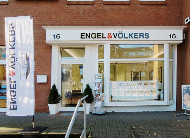 Engel & Völkers real estate office with a brick facade. A white flag with the company logo is on the left. The address "16" is above the entrance.